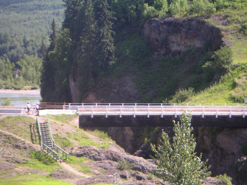 Photo of two cyclists on a distant bridge in the wilderness 